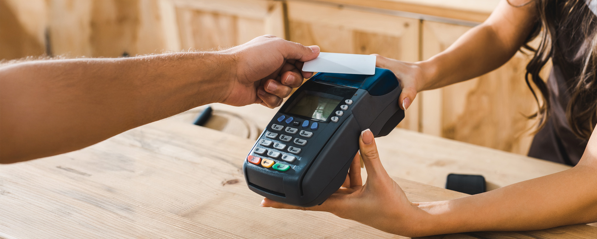 cashier standing near bar counter in brown apron and holding terminal wile man paying with credit card